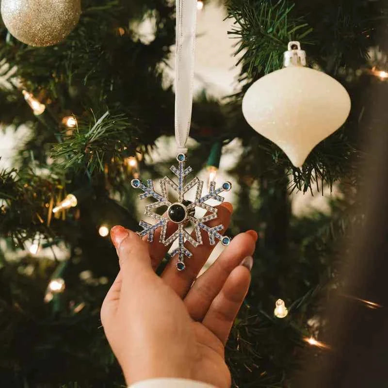 Hand holding personalised blue snowflake photo ornament hanging on Christmas tree with white ribbon